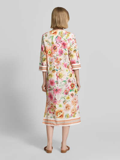 Frauenmodel trägt Tunikakleid im Allover-Look mit V-Ausschnitt von Emily Van den Bergh, bunt gemustert, reine Baumwolle, Ganzkörperansicht Rückansicht.