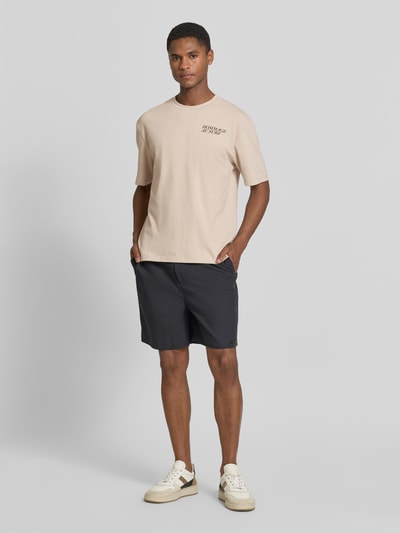 Mannmodel draagt Regular Fit T-shirt aus Baumwoll-Mix van s.Oliver RED LABEL in look: effen kleuren met opschrift, ronde hals, korte mouw, jersey, katoenmix. Ganzkörperansicht van voren.
