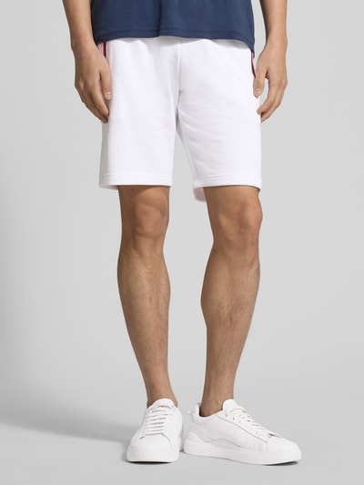 Männermodel trägt Shorts mit elastischem Bund von Christian Berg Men aus weißem Baumwoll-Elasthan-Mix, Regular-Fit, Eingrifftaschen mit Kontraststreifen, Tunnelzug, Innenbeinlänge 23 cm, Bundweite 43 cm, Ganzkörperansicht von vorne.