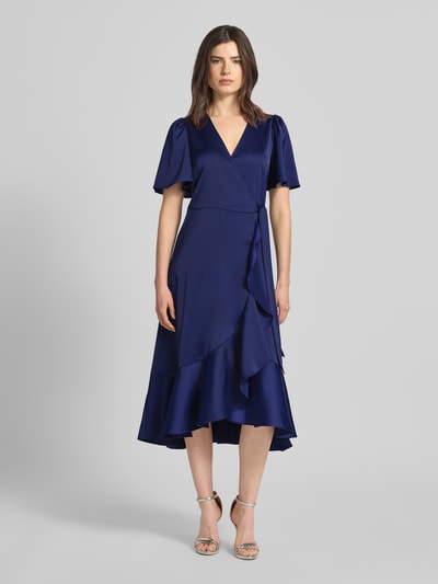 Vrouwenmodel draagt Cocktailjurk met volantzoom model 'THEA' van YAS, satijn, getailleerde fit, midi, wikkel-look, V-hals, vlindermouwen, donkerblauw, vooraanzicht volledige lengte.