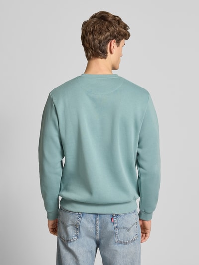 Męski model nosi Sweatshirt mit gerippten Abschlüssen Modell 'BRADLEY' od Jack & Jones, bawełniany materiał, krój regular fit, turkusowy kolor, ściągacze, dżinsowe spodnie, widok całej sylwetki z tyłu.