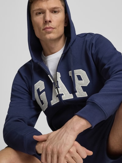 Männermodel trägt Sweatjacke mit Logo und Känguru-Tasche von GAP, dunkelblau, Baumwoll-Mix, Regular-Fit, Nahaufnahme Oberkörper.