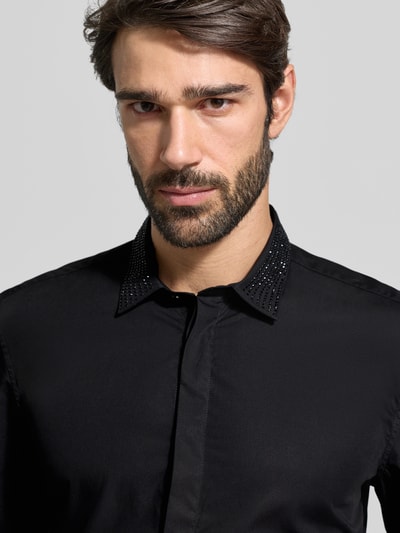 Męski model nosi czarną koszulę casualową Slim Fit Freizeithemd mit Kentkragen Modell 'LONDON' od Antony Morato z bawełny z kentkragen i ozdobnymi kamieniami na kołnierzu, zakryta listwa guzikowa, z przodu, zbliżenie na górną część ciała.