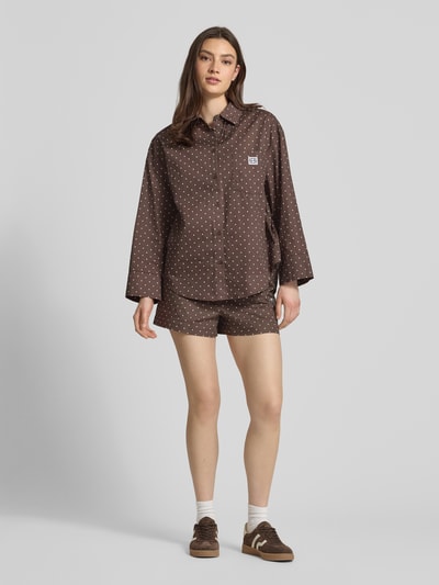 Kobiece modelka nosi szorty z elastycznym pasem i detalem z logo model 'FRIDA' od Noisy May, mieszanka bawełny, krój regular fit, wzór na całej powierzchni, szerokość w rozmiarze S 37 cm, długość wewnętrzna nogawki 9 cm, całopostaciowy widok z przodu.