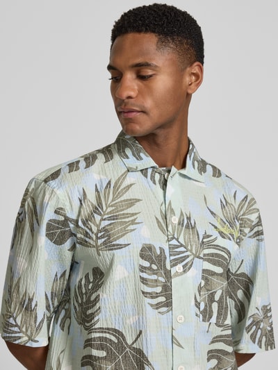 Männermodel trägt Relaxed Freizeithemd mit floralem Allover-Print von Lindbergh in Pastellfarben, halbarm, Kentkragen, Nahaufnahme Oberkörper. Elastischer Baumwoll-Mix, Knopfleiste, strukturierte Textur, Relaxed und Cropped Fit.