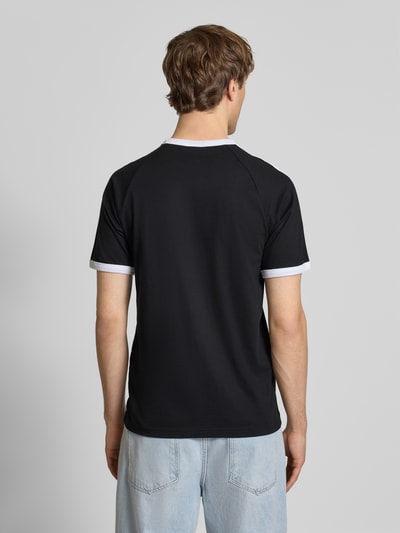 Männermodel trägt T-Shirt mit Label-Stitching von adidas Originals aus reiner Baumwolle, Regular Fit, schwarze Farbe, Ganzkörperansicht Rückansicht.