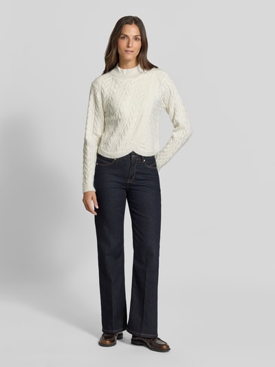 Frauenmodel trägt Strickpullover mit Woll-Anteil in Wickel-Optik von Apricot, Zopfmuster, Stehkragen, cremeweiß, Ganzkörperansicht von vorne.