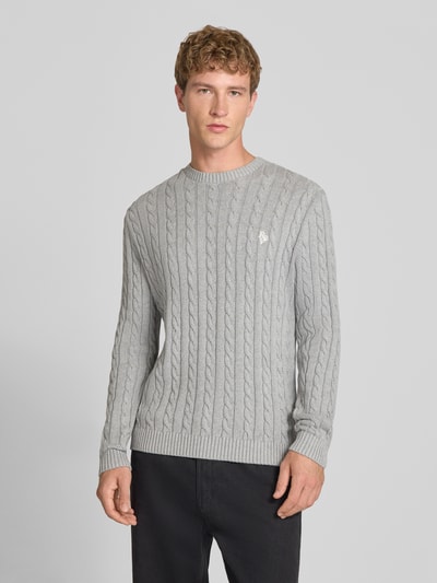 Männermodel trägt Slim Fit Strickpullover reine Baumwolle von REVIEW, hellgrau mit Zopfmuster und Logo-Stickerei, Ganzkörperansicht von vorne.