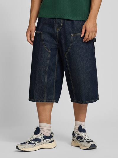 Männermodel trägt Jeans-Bermudas aus reiner Baumwolle Modell 'Double' von Carhartt Work In Progress mit Kontrastnähten, Ganzkörperansicht von vorne. Loose Fit, 5-Pocket-Design, Knopf- und Reißverschluss, Gürtelschlaufen, Bundweite M: 44 cm, Innenbeinlänge M: 41 cm.