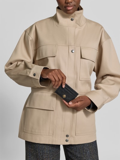 Frauenmodel trägt Kartenetui aus echtem Leder von Tory Burch mit Schlangenmuster, Steppnähten und Metallic-Label, Nahaufnahme Oberkörper.