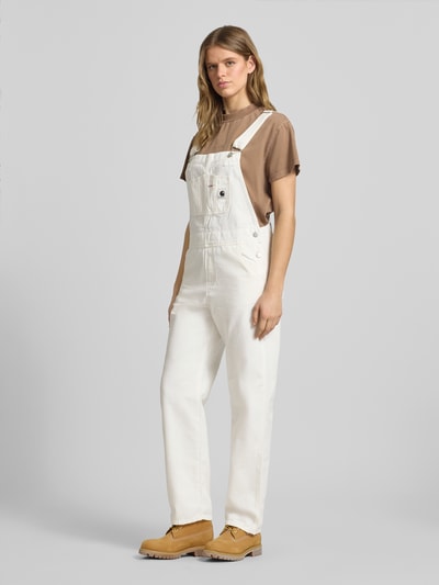 Frauenmodel trägt Overall mit Brusttasche Modell 'BIB' von Carhartt Work In Progress aus Reine Baumwolle in Straight Fit mit Label-Patch, Karree-Ausschnitt, Eingrifftaschen und Gesäßtaschen, helle Farben, Ganzkörperansicht von vorne.