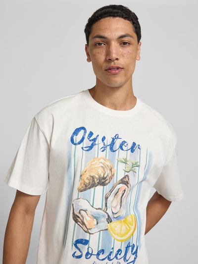 Männermodel trägt T-Shirt mit Motiv-Print von REVIEW in Weiß mit buntem Print, Baumwoll-Mix, Gerader-Schnitt, Rundhalsausschnitt, Nahaufnahme Oberkörper.