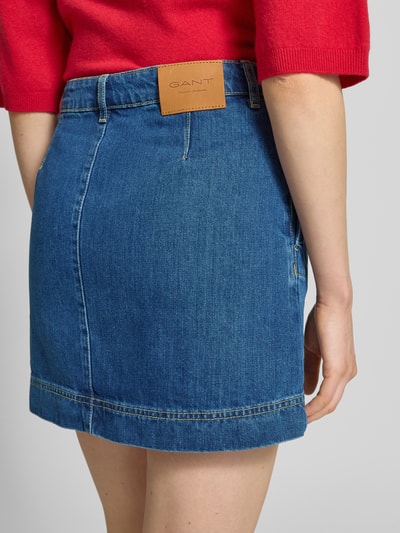 Kobieta nosi Jeansrock aus Baumwolle mit Knöpfen von Gant, niebieska bawełna, prosty krój, spódnica mini, widok z tyłu, detal.