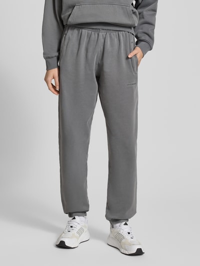 Männermodel trägt High Waist Sweatpants mit elastischem Bund von Pegador, szary bawełniany materiał, elastyczny pas, logo, Ganzkörperansicht von vorne.