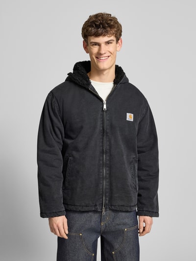 Männermodel trägt Jacke mit Zweiwege-Reißverschluss Modell 'MITCH' von Carhartt Work In Progress aus Baumwolle, Regular Fit, Kapuze, Eingrifftaschen, dunkles einfarbiges Design, Ganzkörperansicht von vorne.