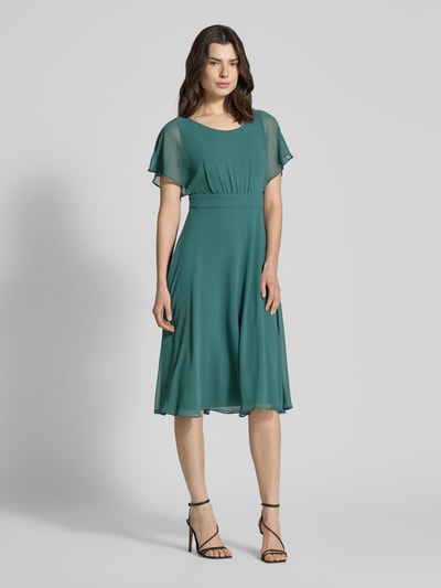 Frauenmodel trägt knielanges Kleid mit Rundhalsausschnitt von Vera Mont in Petrol, semitransparent, tailliert, blickdicht unterlegt, Ganzkörperansicht von vorne.