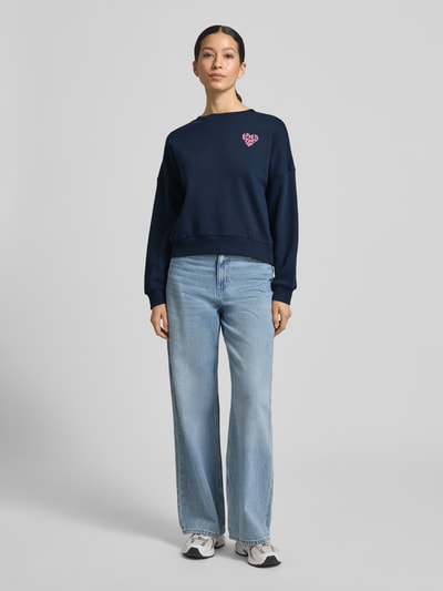 Frauenmodel trägt Regular Fit Sweatshirt aus reiner Baumwolle von Tom Tailor Denim in Dunkelblau, unifarben, Rippenbündchen, Rundhals, Label-Schriftzug, Ganzkörperansicht von vorne.