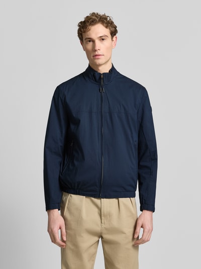 Männermodel trägt Jacke mit Stehkragen Modell 'Calvin' von Brax in Dunkelblau, Reißverschluss, Reißverschlusstaschen, Ganzkörperansicht von vorne. Baumwoll-Mix mit Stretch-Anteil, gerader Schnitt, strukturierte glatte Oberfläche.