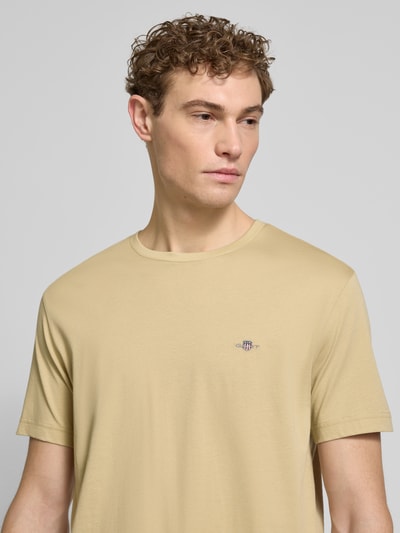 Męski model nosi Regular Fit T-Shirt mit Logo-Stitching od Gant, bawełna, krój regular fit, logo, dekolt okrągły, beż, zbliżenie górnej części ciała.