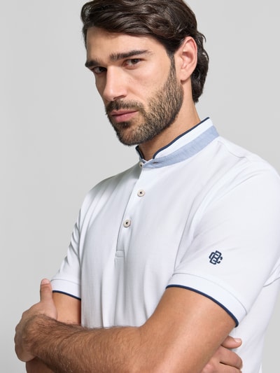Męski model trägt Regular Fit Koszulka polo z bawełny ze stójką i listwą guzikową Christian Berg Men, krótki rękaw, detal gumowego rękawa, długość tyłu 75 cm, kolor biały z niebieskimi akcentami, Nahaufnahme Oberkörper.
