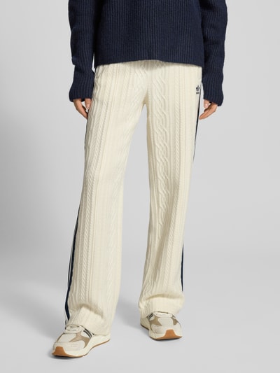Vrouwenmodel draagt Loose Fit Strickhose uit viscosemix van adidas Originals met elastische band, logostitching en galonstrepen, geheelvooraanzicht.