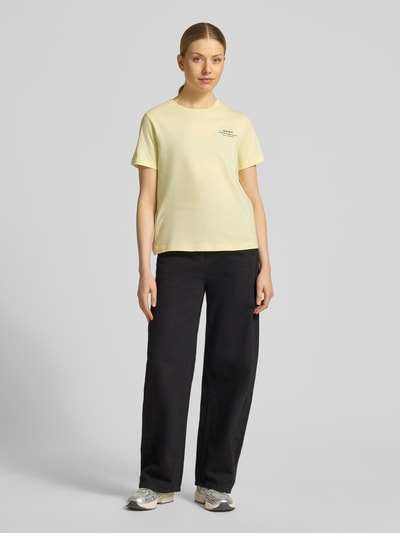 Kobieta nosi T-Shirt mit Label-Print und Rundhalsausschnitt od Gant, damski t-shirt z bawełny, krój regular fit, nadruk z logo, okrągły dekolt, długość tyłu w rozmiarze S: 57 cm, jasny kolor, prosta faktura, gładka powierzchnia, Ganzkörperansicht von vorne.