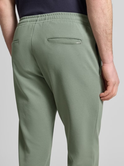 Mężczyznamodel nosi Regular Fit Hose mit elastischem Bund von Antony Morato, mieszanka bawełny, długość wewnętrzna nogawki 76 cm, szerokość w rozmiarze M: 41 cm, pas elastyczny, szwy pionowe, spodnie zielone, tekstura gładka, materiał miękki, widok całej sylwetki z tyłu