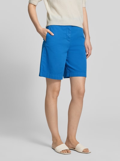 Frauenmodel trägt Regular Fit Chino-Shorts aus Baumwoll-Lyocell-Mix von Tommy Hilfiger, efekt: jednolity kolor, wpuszczane kieszenie, wyhaftowane logo, krój regular fit, mieszanka bawełny i lyocellu, zapięcie na guzik i zamek błyskawiczny, widoczne szwy, gładka faktura, Ganzkörperansicht von vorne.