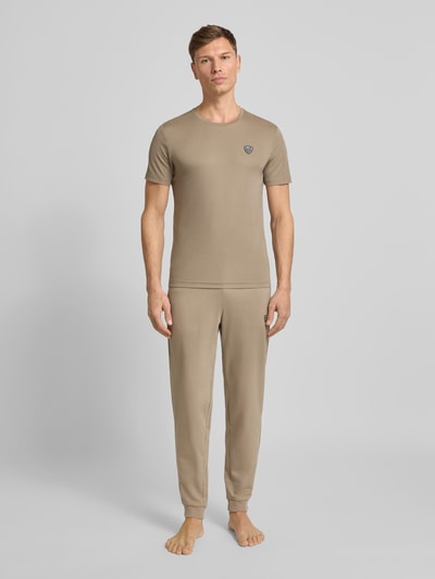Mężczyznamodel nosi Spodnie dresowe z logo i elastycznym pasem od EA7 Emporio Armani, mieszanka bawełny i elastanu, krój regular fit, długość wewnętrzna 74 cm, beżowy kolor, gładka tekstura, całopostaciowy widok z przodu.