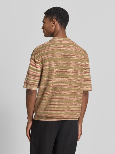 Männermodel trägt Relaxed Fit Poloshirt aus reiner Baumwolle Modell 'Muse' von SELECTED HOMME mit gestreiftem Allover-Muster, Strickstruktur in Grün- und Beigetönen, Rumpfabschluss und Ärmelabschluss gerippt, Ganzkörperansicht Rückansicht.