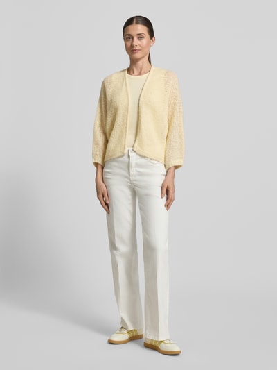 Frauenmodel trägt Relaxed Fit Cardigan mit Baby-Alpaka-Anteil Modell 'Tulea' von Someday im sanften Gelb, Strick-Optik, Material-Mix, Rückenlänge 51 cm, Ärmellänge 49 cm, kombiniert mit heller Hose, Ganzkörperansicht von vorne.