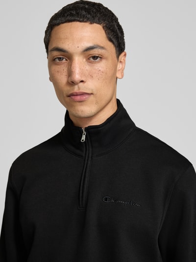 Männermodel trägt Sweatshirt mit Label-Details von Champion in Schwarz, Troyer-Kragen, Baumwollmischung, Nahaufnahme Oberkörper.