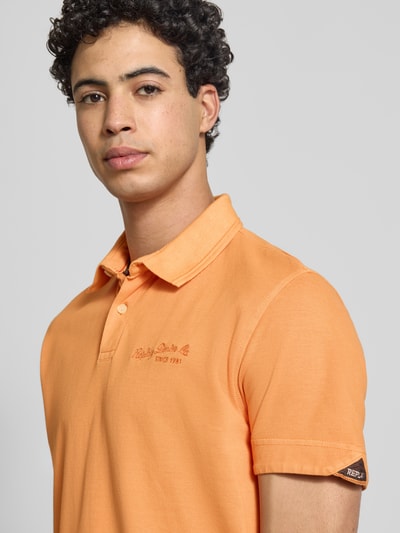 Männermodel trägt Regular Fit Poloshirt aus reiner Baumwolle von Replay, Label-Stitching, orange, Kurzärmelig, Nahaufnahme Oberkörper.