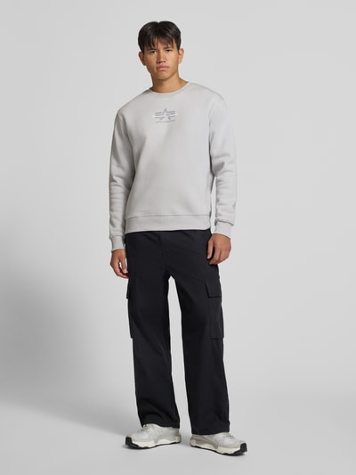 Männermodel trägt Regular Fit Sweatshirt aus Baumwoll-Mix mit Label-Detail von Alpha Industries, helle Farbe, elastische Abschlüsse, Ganzkörperansicht von vorne.