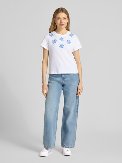 Kobiece model nosi damski t-shirt z haftami i perłami od Rich & Royal, bawełna, krój regular fit, okrągły dekolt, długość tyłu 54 cm, jasne kolory, widok całej sylwetki z przodu.
