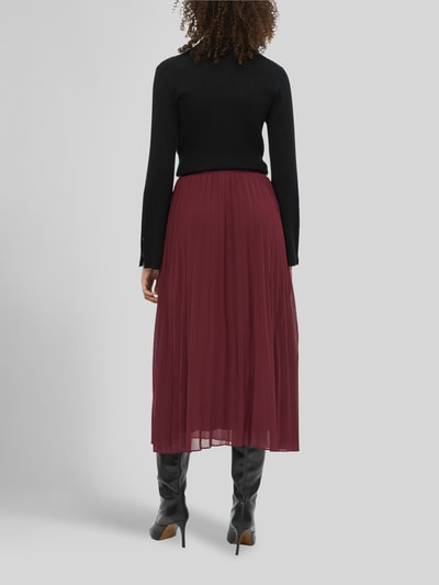 Frauenmodel trägt Plisseerock mit schwingendem Volantsaum von S. OLIVER BLACK LABEL in Bordeaux, unifarben, Midi-Länge, Falten, Volant, Ganzkörperansicht Rückansicht.