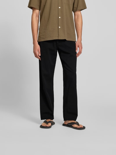 Männermodel trägt Straight Fit Jeans mit elastischem Bund von Forét in Schwarz, reine Baumwolle, sichtbar Gesäßtaschen, Ganzkörperansicht von vorne.