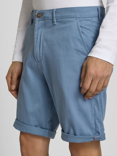Mężczyzna nosi Regular Fit Shorts mit Eingrifftaschen Modell 'BOWIE' od Jack & Jones, bawełniano-elastanowe, kolor jasnoniebieski, krój regular fit, kieszenie z przodu, podwijane nogawki, szerokość w rozmiarze M: 43 cm, długość nogawki od kroku w rozmiarze M: 26 cm, zbliżenie na dolną część ciała z przodu