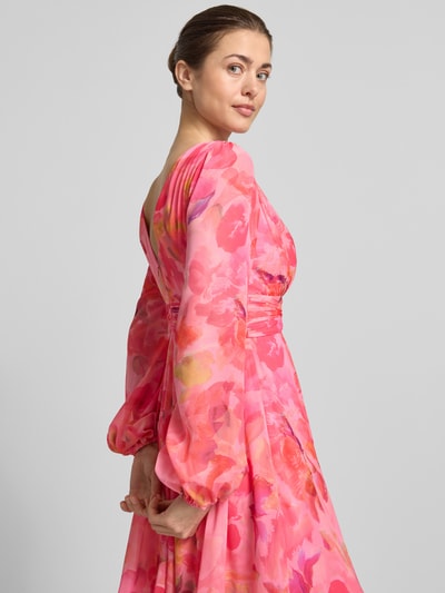 Frauenmodel trägt Cocktailkleid mit Ballonärmeln und V-Ausschnitt von Jake*s Cocktail aus Chiffon, taillierter Schnitt, farbenfrohes Minikleid mit floralen Rosa- und Pinktönen, Rückseitiger V-Ausschnitt und Rückenreißverschluss, Rückenlänge 91 cm, Brustweite 40 cm, Ärmellänge 65 cm, Nahaufnahme Oberkörper.