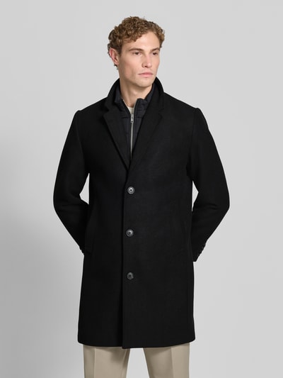 Männermodel trägt Mantel mit Knopfleiste von Lindbergh in Schwarz, gerade Passform, Reverskragen, Eingrifftaschen, Ganzkörperansicht von vorne.