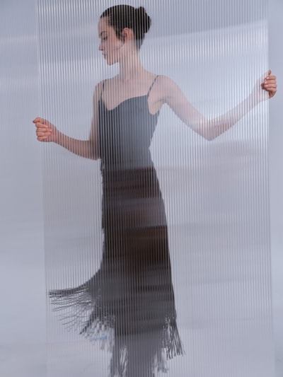 Frauenmodel trägt Midikleid mit Ausfransungen von Rabanne, schwarzer Acetat-Mix, tailliert, Spaghettiträger, Ganzkörperansicht von vorne.