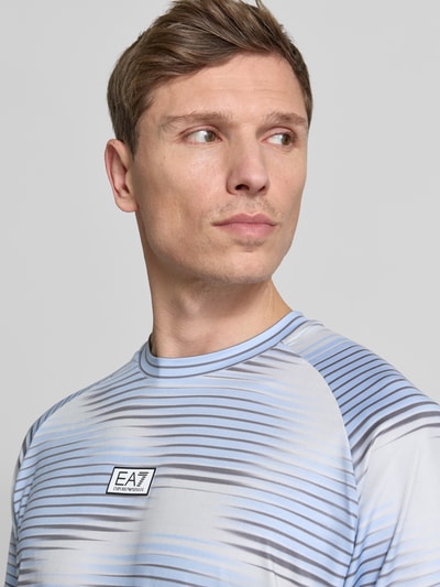 Männermodel trägt Regular Fit T-Shirt mit Logo-Applikation von EA7 Emporio Armani in Grau und Blau, elastischer Material-Mix, Nahaufnahme Oberkörper.
