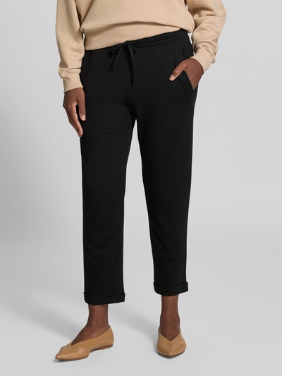 Frauenmodel trägt Sweatpants in verkürzter Passform von Juvia, schwarz, Baumwoll-Modal-Mix, elastischer Bund, Eingrifftaschen, Ganzkörperansicht von vorne.