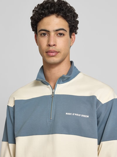 Męski model nosi Relaxed Fit Troyer aus reiner Baumwolle von Marc O'Polo Denim, wzór paski, niebiesko-kremowe kolory, bawełna, zbliżenie na górną część ciała.
