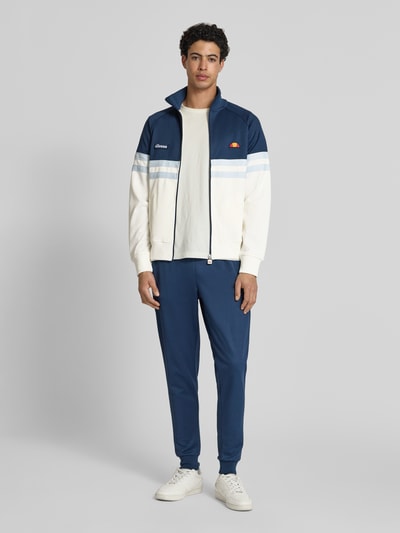 Męski model nosi bluzę rozpinaną z mieszanki bawełny model 'RIMINI' od Ellesse, prosty krój, stójka, detale z logo, granatowo-biała, całkowity widok z przodu