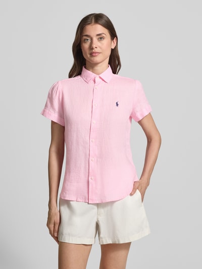 Modelka kobieca nosi Regular Fit Leinenbluse aus reinem Leinen von Polo Ralph Lauren w jednolitym jasnoróżowym kolorze, lniana tekstura, logo na piersi, krótki rękaw, kołnierz koszulowy, zapięcie na guziki, przód, krój regular fit, widok całej sylwetki z przodu.
