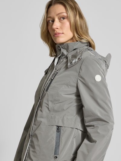 Vrouwenmodel draagt Jacke mit Kapuze und Eingrifftaschen van Gil Bret in regular fit, grijs met ritszakken, knoopsluiting, weather protection, ruglengte maat 36: 67 cm, schouderbreedte maat 36: 40 cm, borstwijdte maat 36: 46 cm, mouwlengte maat 36: 64 cm. Nahaufnahme bovenlichaam.