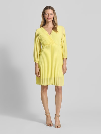 Frauenmodel trägt knielanges Kleid mit Plisseefalten Modell 'Im44sa' von ZABAIONE in Gelb, Wickel-Optik, taillierter Schnitt, Ganzkörperansicht von vorne.