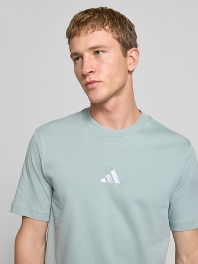 Männermodel trägt T-Shirt mit Logo und Rundhalsausschnitt von adidas Sportswear aus reiner Baumwolle in Hellblau, Nahaufnahme Oberkörper.