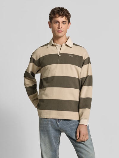 Männermodel trägt Sweatshirt mit Label-Stitching von Forét in Beige und Oliv, gerade geschnitten, Polokragen, Ganzkörperansicht von vorne. Rückenlänge bei Größe M: 72 cm, überschnittene Schultern.